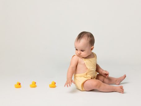 Bebé sentado en el suelo observando patitos de goma amarillos.