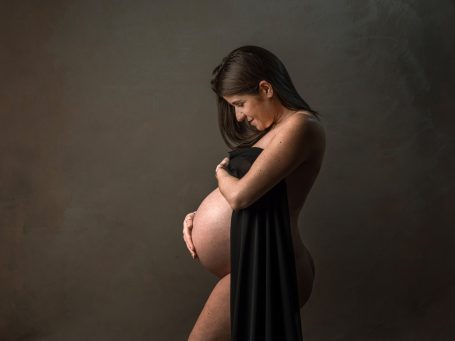 Mujer embarazada posando de perfil, cubierta parcialmente con una tela negra.