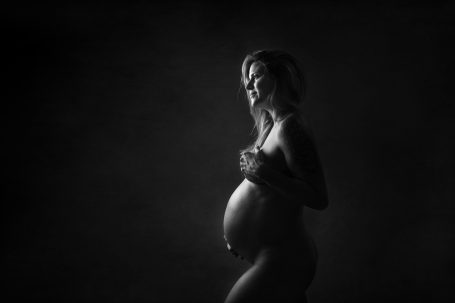 Mujer embarazada en silueta, con fondo oscuro, sosteniendo su barriguita.