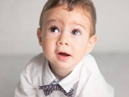 Niño pequeño, vestido con camisa y pajarita, mirando hacia arriba con curiosidad.