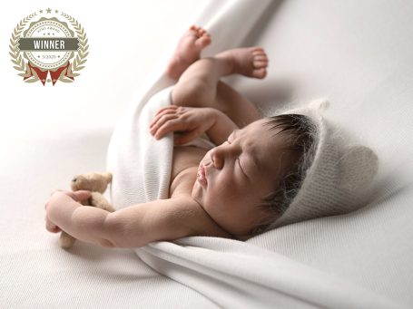 Bebé dormido envuelto en una manta, con gorro blanco y juguete en la mano.