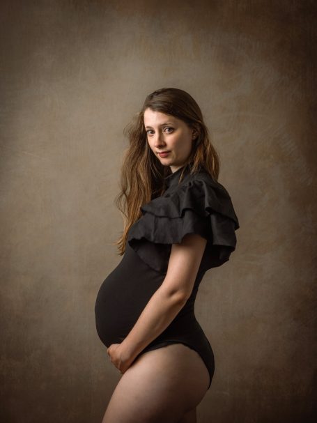 Mujer embarazada con vestido negro, posando de perfil y sosteniendo su barriga.