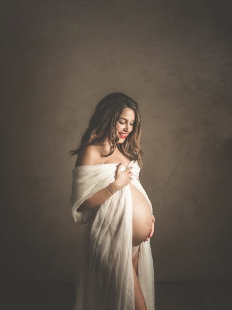 Mujer embarazada sonriendo, vestida con una tela blanca que cubre su cuerpo.