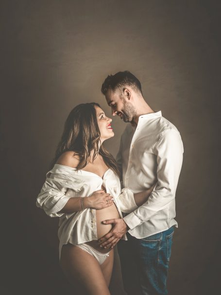 Pareja sonriente en un momento íntimo, la mujer embarazada acaricia su vientre.