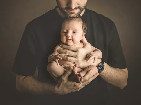 Hombre sosteniendo a un bebé con una expresión sonriente en un entorno oscuro.