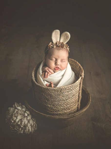 Bebé dormido en una cesta, envuelto en una manta y con orejas de conejo.