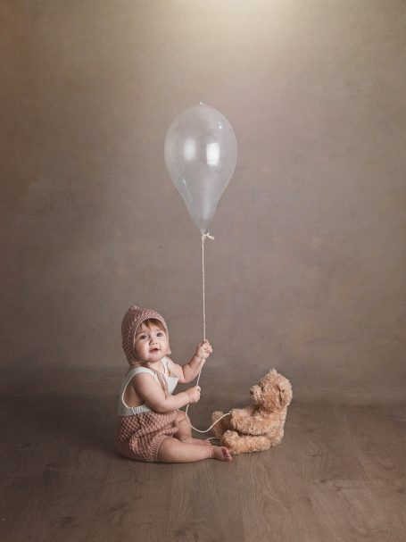 Niño sentado con un globo y un oso de peluche en un ambiente suave y iluminado.