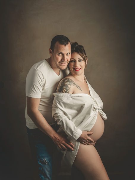Pareja sonriente en un retrato, con la mujer embarazada mostrando su barriga.