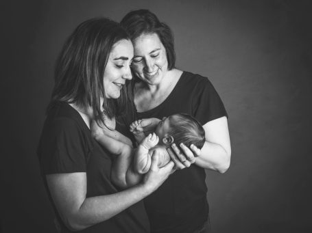 Dos mujeres sonríen mientras sostienen a un bebé en un entorno con luz suave.