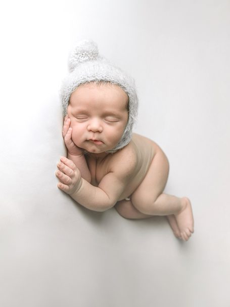 Bebé dormido con gorro blanco, recostado sobre una superficie clara.