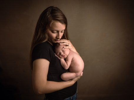 Mujer sosteniendo a un bebé recién nacido con ternura en un ambiente suave.