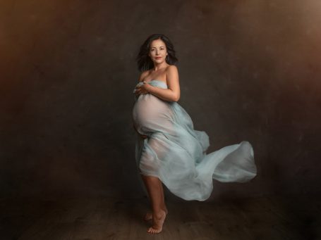 Mujer embarazada posando con un vestido fluido en un entorno difuso y cálido.