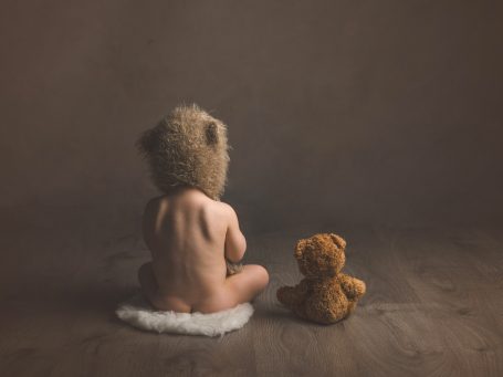 Niño de espaldas con un gorro de oso, junto a un oso de peluche.