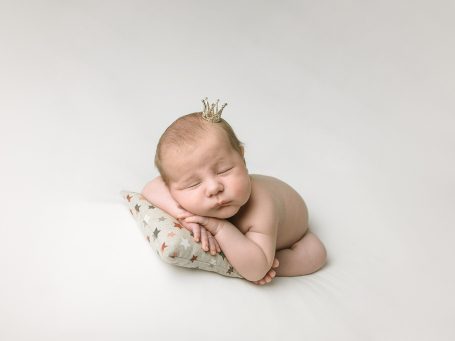 Bebé durmiendo sobre un cojín, con una diadema pequeña en la cabeza.