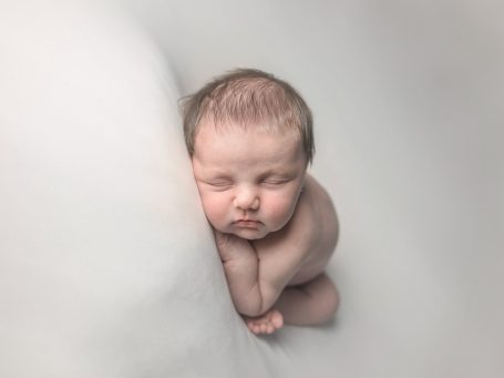 Bebé dormido en posición fetal sobre fondo suave y claro.