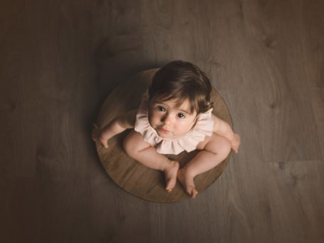 Bebé sentado sobre una alfombra, mirando hacia arriba con expresión curiosa.