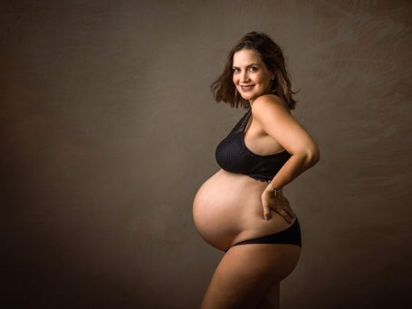 Mujer embarazada sonriendo, de perfil, con un fondo suave y neutro.