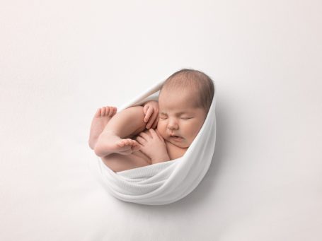 Bebé durmiendo envuelto en una tela blanca, con las piernas recogidas.