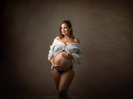 Mujer embarazada sonriendo, con una camisa blanca y las manos en la barriga.