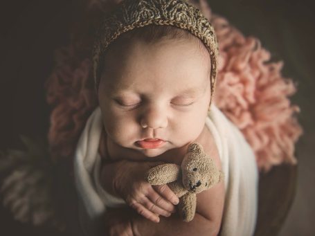 Bebé dormido con un osito de peluche, rodeado de flores suaves.