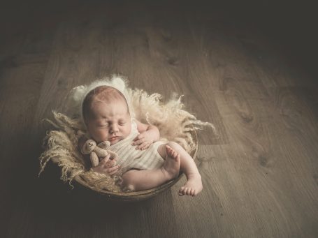 Bebé dormido en un cesto decorado con paja, sobre un suelo de madera.