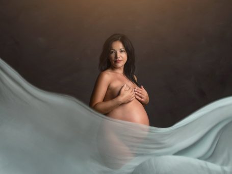 Mujer embarazada posando de forma artística con tela flotante alrededor.