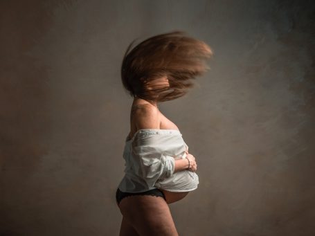 Mujer embarazada con cabello al viento, sosteniéndose el vientre.