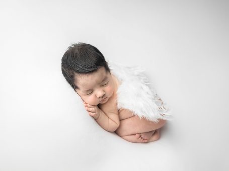 Bebé dormido con alas de ángel sobre un fondo blanco.