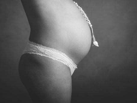 Barriga de embarazada de perfil, con encaje claro y fondo oscuro.